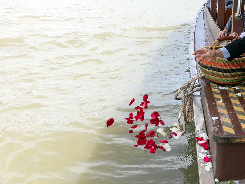 Bestattungsarten: Seebestattung mit Rosenblättern – Schwarz & Sohn Rote Rosenblätter werden von einem Boot aus auf das Wasser gestreut – Symbolbild einer Seebestattung.